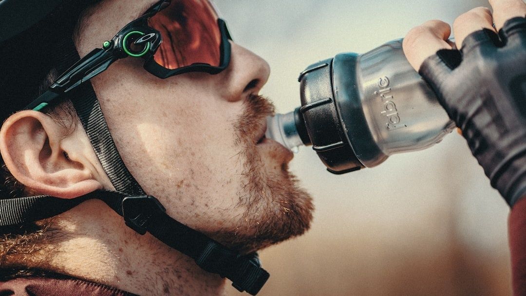 Ausdauerathlet mit Sonnenbrille trinkt beim Sport aus einer Flasche
